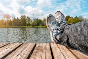 Man with crossed legs relaxing on the wooden pier during beautiful spring day