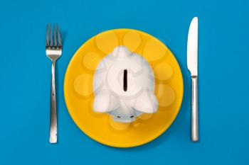 Piggy bank with a fork and knife on the plate. Eat up savings, savings consumer concept