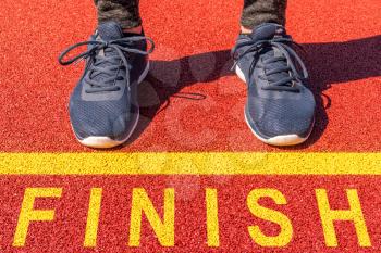 A pair of feet standing at the edge of a yellow line on an running track with a yellow print of the word Finish. Concept of accomplishment.