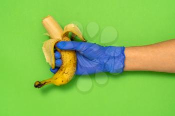 Female hand in medical glove holds yellow bitten banana over green background