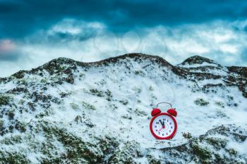 Frozen time. Alarm clock on a rock covered by snow. Extreme weather situation. Winter time.