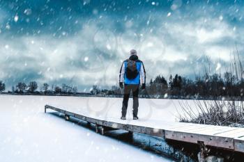 Man standing on the frozen lake pier at snowy weather