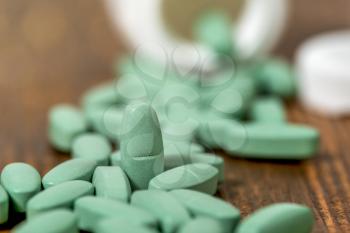 Green medical pills spilling out of a drug bottle