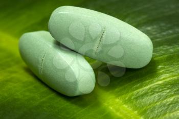 Herbal medicine capsules pills on green organic herb leaf