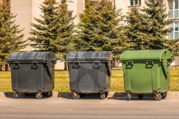 Three plastic garbage standard containers lined up on the street