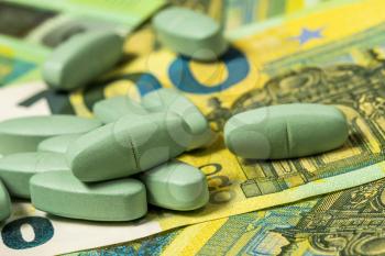 Green pills over euro banknotes. Money, healthcare and drug trafficking concept.