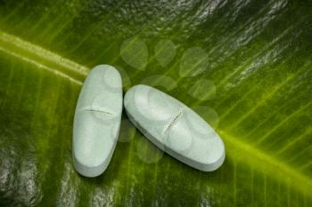 Herbal medicine capsules pills on green organic herb leaf. Alternative medicine concept.