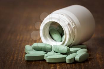 Green medical pills spilling out of a white bottle