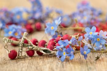 Forget-me-not flowers and Christian cross with rosary on the wooden background. Close up view.