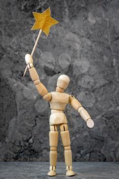 Wooden mannequin posing with a golden star in a hand. Celebration concept.