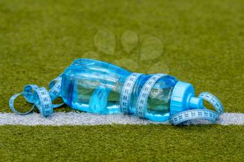 Plastic bottle of water with measure tape on green artificial grass at football field