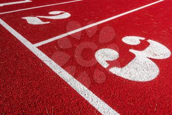 Numbers on start point of running track background. Red running track in stadium. 