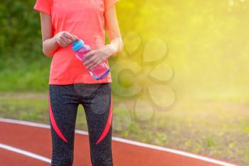 Sporty girl with bottle of water outdoors. Girl resting after training at sport stadium. Healthy lifestyle concept.