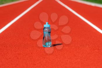 Thirst and water balance concept. Bottle of water on running track on the stadium.
