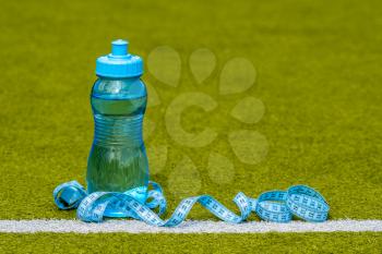 Bottle of water and measure tape  on green football field