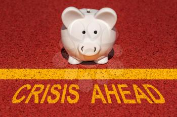 Financial crisis ahead - piggy bank at the edge of a yellow line with a yellow print of the message CRISIS AHEAD
