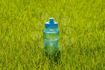 Sport blue plastic water bottle in the grass of football stadium