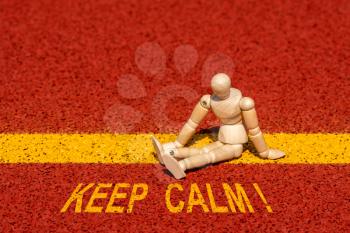 Wooden man sitting at the edge of a yellow line with a yellow print of the message KEEP CALM