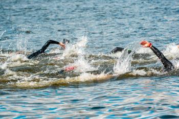 Triathlon swimmers in the water. Swimmers swim during swimming competition in the lake. Unrecognizable persons.