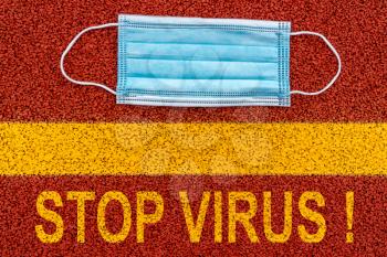 Medical disposable face mask on the ground with yellow print of the message STOP VIRUS