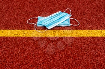 Medical masks lying behind the yellow line in the sports ground. Stay safe concept. Cancellation of sports competitions due to the virus.