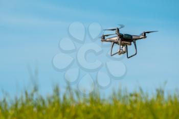 Drone quadcopter hovering over grass field on sunny day