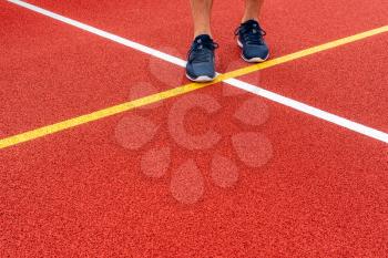 A pair of sports athlete feet standing on a red color game court.