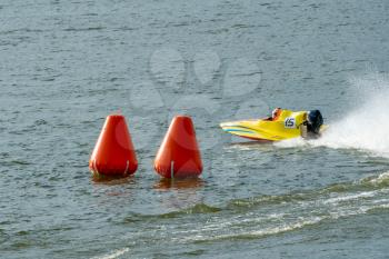 Yellow powerboat go fast along the lake and rounding a marker buoy in a race. Focus on orange buoy.