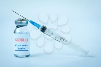 Small vaccine bottle  with a label that read Covid - 19 Coronavirus Vaccine  & a medical syringe. Vaccination for prevention, immunization & treatment to virus