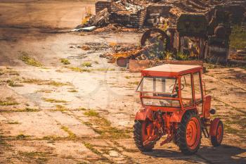 Red tractor parked in the yard of abandoned factory 