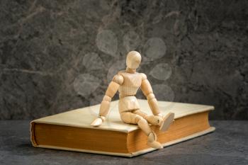 Wooden man sitting on the book. Literature research. Concept - information search in books. 