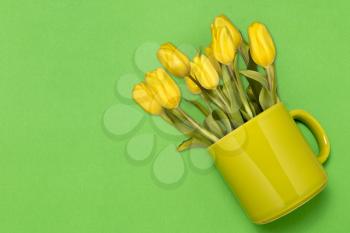 Creative layout made of coffee or tea cup with yellow tulips on green  background