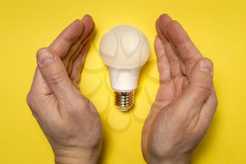 A concept image of a new idea, new birth. Hands covering led lightbulb.