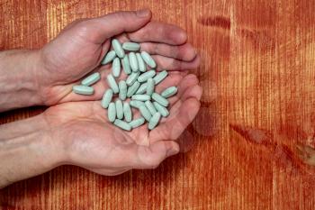 Medicine pills or capsules in hands over wooden background
