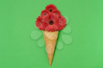 Ice cream cone with flowers on green background. Summer flowers concept