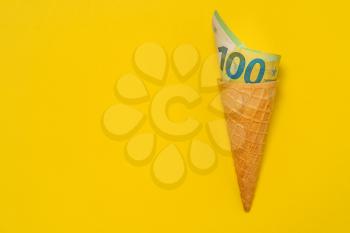 Ice cream wafer cone with rolled up euro banknote. Euro bill rolled in ice cream cone. Copy space.