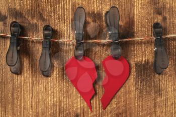 Broken paper heart hangs on clothespins on a wooden background