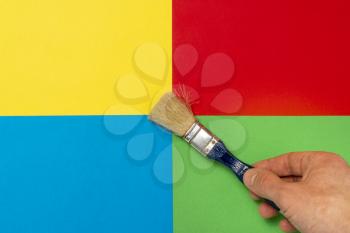 Hand with paint brush on the colored paper background. Creativity concept.