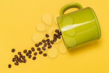 Spilled coffee beans from the green ceramic cup  on the yellow background