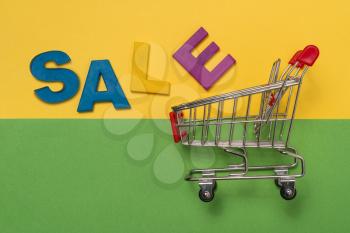 Empty shopping cart and inscription SALE on color paper background