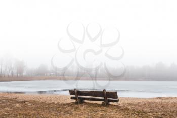 Empty bench at the frozen lake in the fog 