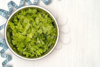 Salad with fitness measuring tape over wooden background. Diet Food and healthy lifestyle concept.