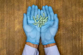 The doctor or pharmacist in blue gloves holding capsules in her hands