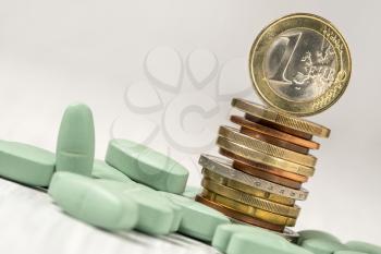 Stack of coins with pills on the table, close up view. Healthcare costs or financial aid concept.