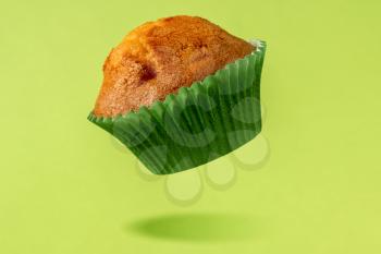 Muffin in a baking paper cup levitating over a green background