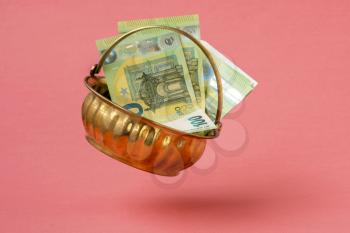 Golden pot full of Euro currency falling on pink background
