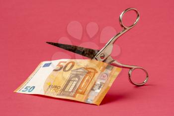 Cutting fifty Euro with scissors on pink background. Concept on the topic of devaluation of money. 