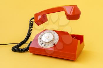 Retro orange telephone with the receiver raised, isolated on yellow background