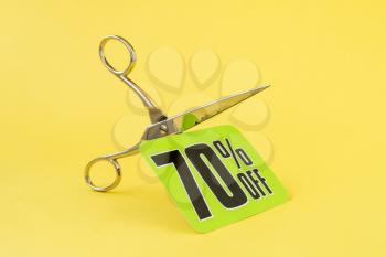 Scissors cutting the price tag on the yellow background. Cutting price or sale concept.