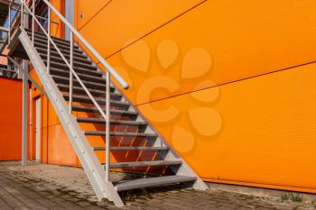 Iron staircase for up to maintenance work or fire escape. Metal stairs are on the side of the orange wall.